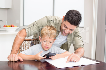 Smiling father helping son with math homework at table