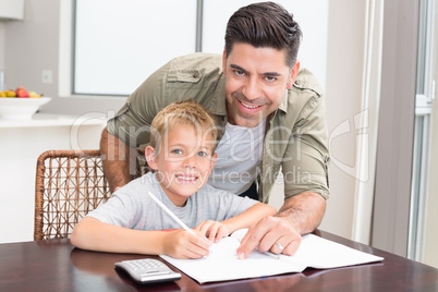 Cheerful father helping son with math homework at table