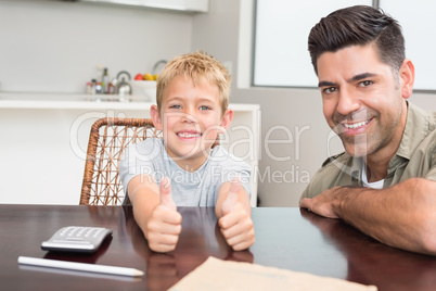 Father and son giving thumb up smiling at camera at the table