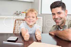 Father and son giving thumb up smiling at camera at the table