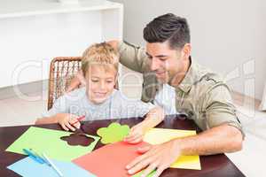 Father and son making paper shapes together at the table