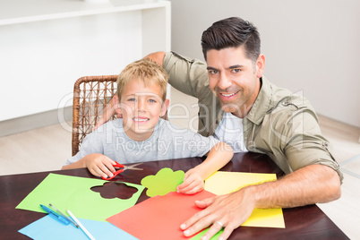 Happy father and son making paper shapes together at the table