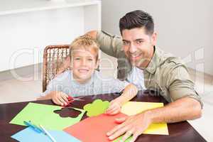 Happy father and son making paper shapes together at the table