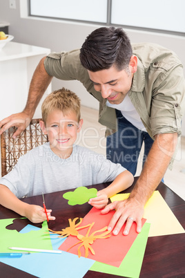 Father and smiling son making paper shapes together at the table