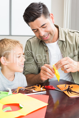 Cheerful little boy making paper shapes with father at the table