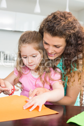 Little girl making paper shapes with mother at the table