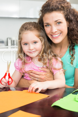 Happy little girl making paper shapes with mother at the table
