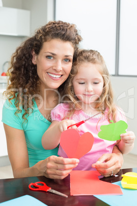 Cute little girl cutting paper shapes with mother at the table