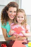 Cute little girl showing paper heart sitting on mothers lap