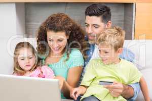 Cheerful family sitting on sofa with laptop shopping online