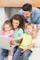 Cheerful family sitting on sofa looking at laptop