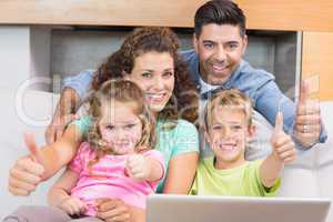 Happy family sitting on sofa using laptop giving thumbs up