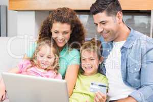 Happy family sitting on sofa using laptop together to shop onlin