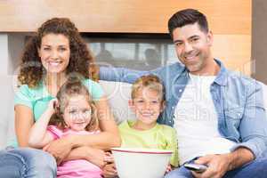 Happy family sitting on sofa watching tv with popcorn