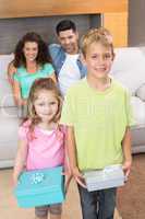 Siblings holding presents in front of parents on the couch