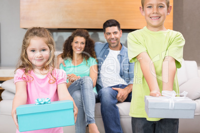 Siblings showing presents in front of parents on the couch