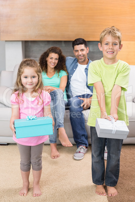 Happy siblings showing presents in front of parents on the couch Happy siblings showing presents in front of parents on the couch