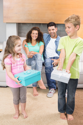 Happy siblings holding presents in front of parents on the couch