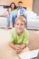 Smiling little boy using laptop on the rug with parents sitting