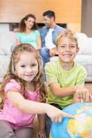 Smiling siblings pointing to globe on the rug