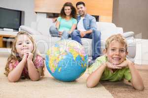 Smiling siblings lying on the rug with a globe