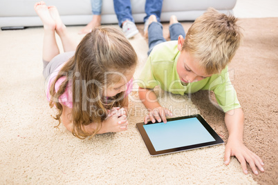 Smiling siblings lying on the rug using a tablet