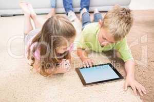 Smiling siblings lying on the rug using a tablet