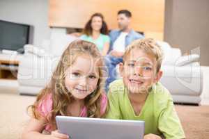 Happy siblings lying on the rug using a tablet