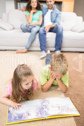 Happy siblings lying on the rug reading a storybook