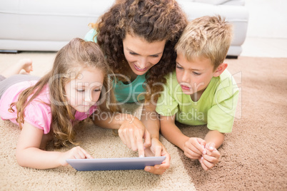 Happy siblings lying on the rug using tablet with their mother