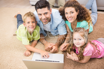 Happy siblings lying on the rug using laptop with their parents