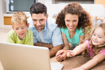 Cute siblings lying on the rug using laptop with their parents