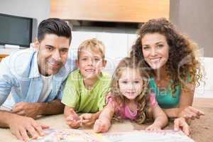 Happy siblings lying on the rug reading storybook with their par