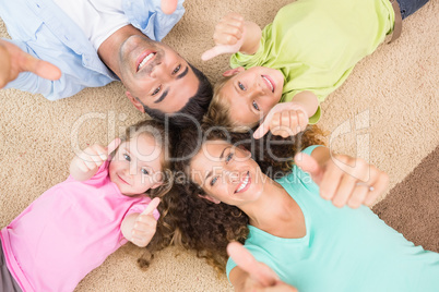 Smiling family lying on the rug in a circle showing thumbs up