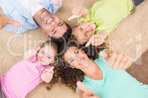 Smiling family lying on the rug in a circle showing thumbs up
