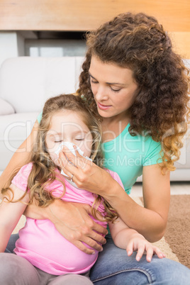 Caring mother helping her little daughter blow her nose