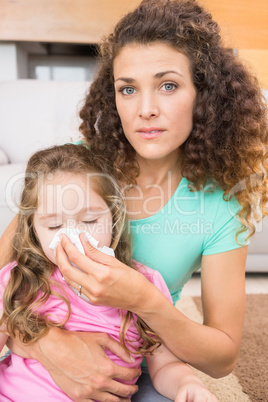 Worried mother helping her little daughter blow her nose