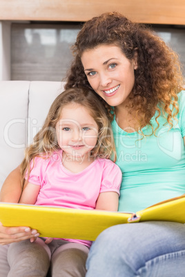 Pretty mother sitting with her little daughter reading a storybo