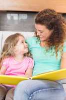 Happy mother sitting with her little daughter reading a storyboo