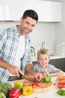 Happy father teaching his son how to chop vegetables