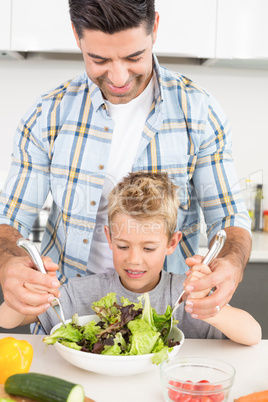 Smiling father tossing salad with his son