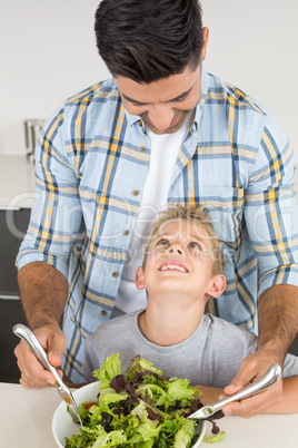 Smiling father tossing salad with his little son