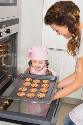 Mother taking cookies out of the oven with little girl watching