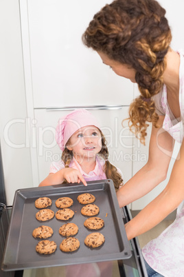 Mother taking cookies out of the oven with daughter pointing at