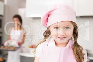 Little girl wearing pink apron and chefs hat smiling at camera