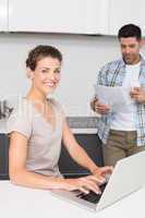 Smiling woman using laptop while partner reads the newspaper