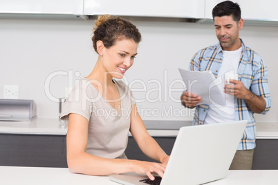 Pretty woman using laptop while partner reads the newspaper