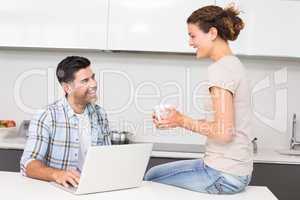 Happy man using laptop while partner sits with a coffee