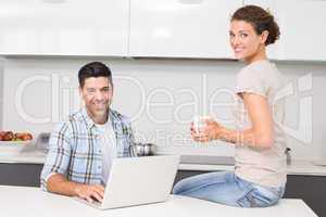 Smiling man using laptop while partner sits with a coffee