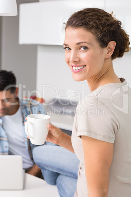 Cheerful woman drinking coffee while partners uses laptop